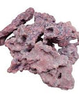 A pile of AO - Premium Reef Rock Asst., characterized by rugged, jagged pinkish-red surfaces and irregular forms, arranged against a plain white background.