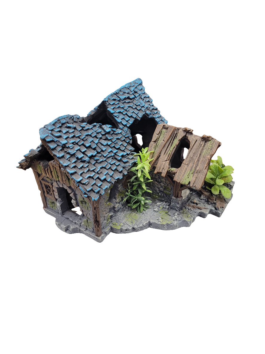 The Blue Roof Dilapidated Cottage Decor is an 8x8 inch, 5.5-inch-tall model of a weathered house featuring broken wooden beams and small green plants on a textured base.