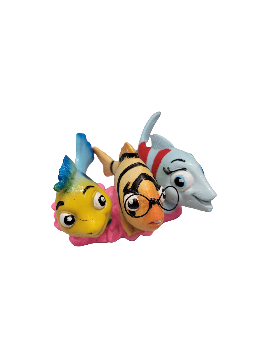 The Hikari - Weird Waters Sprats Decor features a trio of vibrant cartoon fish on a pink base: a yellow fish with blue fins, a brown and orange-striped fish with glasses, and an open-mouthed light blue shark.