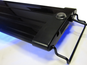 Close-up of the Aquarium Masters - Advance LED Lighting Systems 48 in black, showcasing its sleek rectangular design and LED technology for optimal color rendition. It features a circular button and vent-like slots at one end, with two metal hooks on the edges and a soft blue glow from below.