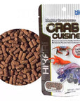 The Hikari Crab Cuisine package (1.76oz) shows brown, sinking sticks and images of a crab and hermit crab. It highlights its benefits for crustaceans, focusing on calcium content to support shell development.
