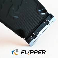 Close-up of the Flipper - Max Replacement Blades Large, featuring a black razor blade with a silver edge, positioned diagonally on a white background. The word FL!PPER is below, flanked by two stylized dolphin icons in blue and orange.