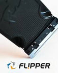 Close-up of the Flipper - Max Replacement Blades Large, featuring a black razor blade with a silver edge, positioned diagonally on a white background. The word FL!PPER is below, flanked by two stylized dolphin icons in blue and orange.
