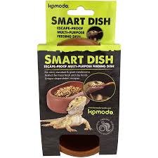 Packaging for Komodo - Smart Dish shows a lizard beside the escape-proof, multi-purpose dish. Predominantly green and brown, the package includes a circular cutout at the bottom.