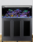 The Innovative Marine INT 150 Lagoon Aquarium with APS Stand displays vibrant coral reefs and colorful fish atop a sleek black cabinet against a light wall, accompanied by a wooden cabinet and red chair, featuring the Trapezoid Infinity Overflow system for seamless water flow.