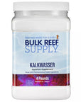 A container of Bulk Reef Supply Pharma Kalkwasser (Calcium Hydroxide), a supplement for reef aquariums, prominently displays on its label that it is made with pharmaceutical-grade calcium hydroxide and has a weight of 4 pounds. The background features a stunning illustration of vibrant reefs and coral patterns.