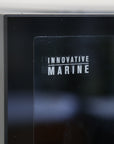 Close-up of a black glass panel featuring INNOVATIVE MARINE in white capitals. The reflection suggests its part of the Innovative Marine- EXT 200 Aquarium w/ APS Stand, designed for displaying your 200-gallon aquarium.