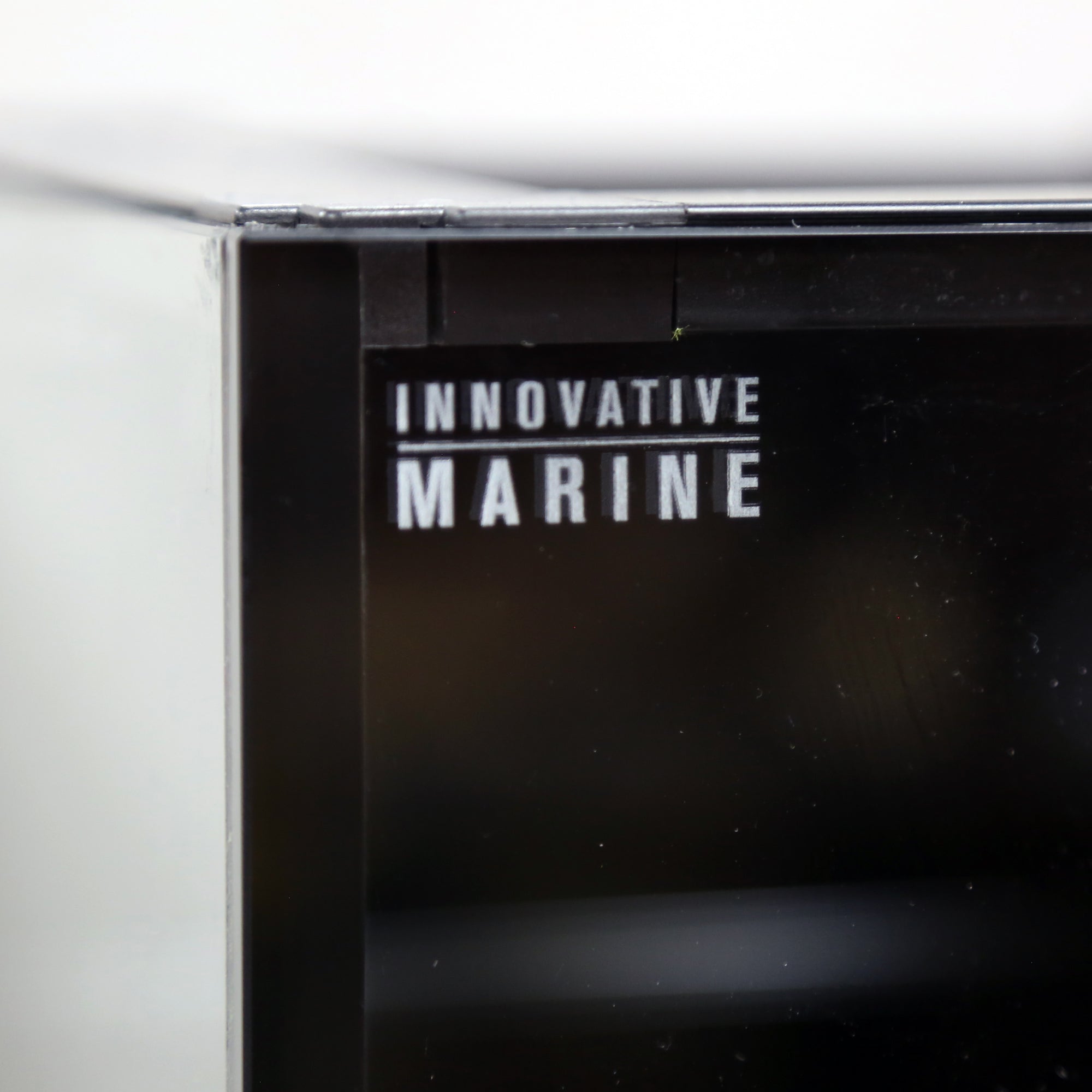 Close-up of a black display corner with the text Innovative Marine, showcasing the sleek, modern design of the Innovative Marine -INT 200 Gallon Complete Reef System stand. Its reflective surface and sharp edges enhance any saltwater reef system.