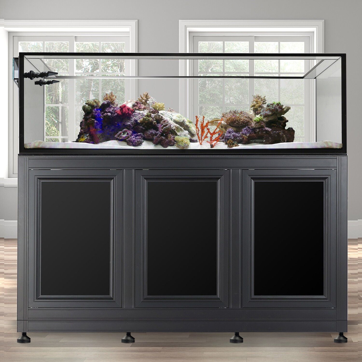 An Innovative Marine - EXT 200 Peninsula Aquarium w/ APS Stand stands against a light gray wall. Vibrant coral decorates white sand inside, with colorful corals of the NUVO EXT system adding vibrancy.