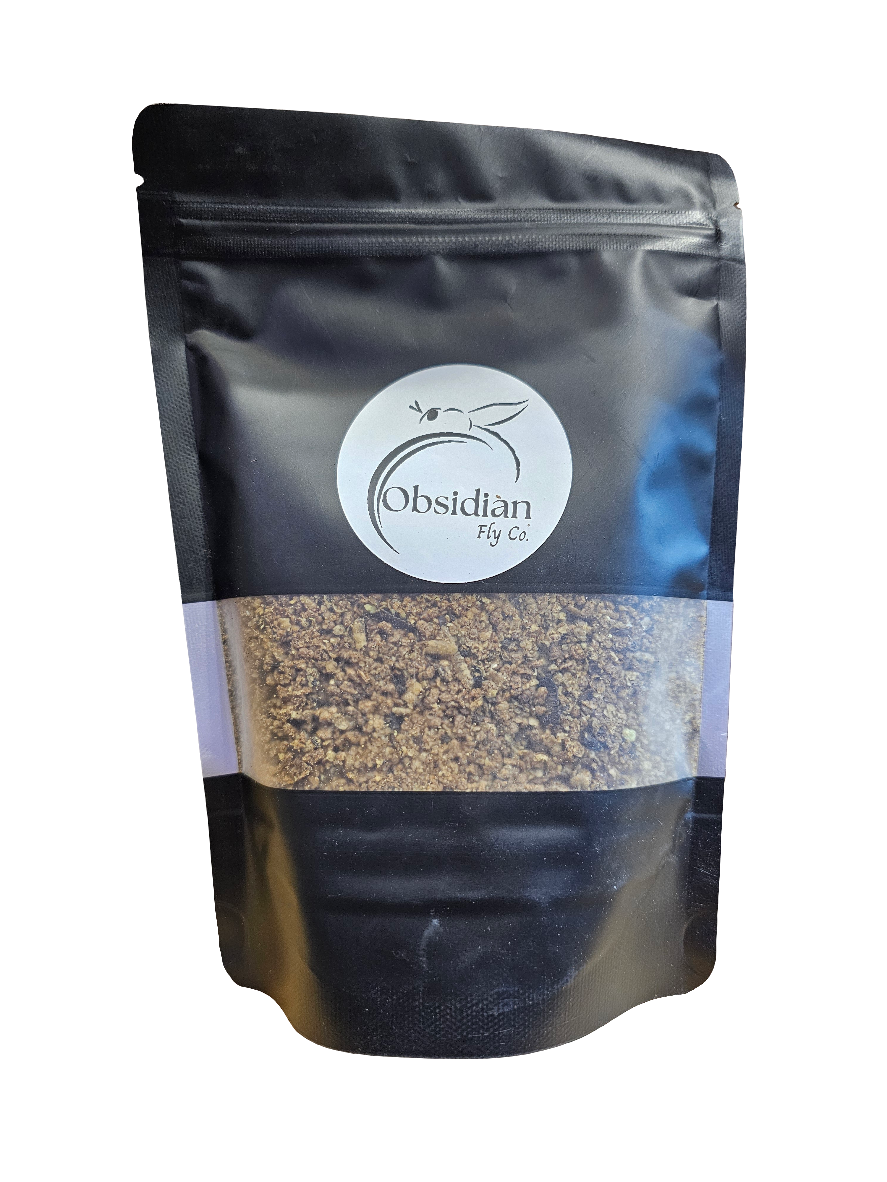 A black resealable pouch labeled Obsidian Fly Co. - Black Soldier Fly Larvae - Larval Crumble 6 Oz contains a sandy, textured substance visible through a transparent section in the middle.