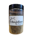 A clear jar with a black lid contains brown powder and is labeled Obsidian Fly Co. - Black Soldier Fly Larvae - Larval meal 3 oz, featuring a fly graphic above the text.