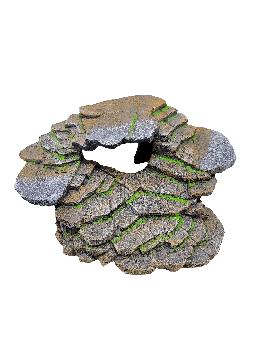 The Reptology - Ledge & Cave Hide features a miniature rocky terrain piece with layered stone slabs and a central hole. The stones are crafted with texture, showcasing shades of gray and brown, along with patches of green moss, creating a design that resembles a circular, natural rock formation.