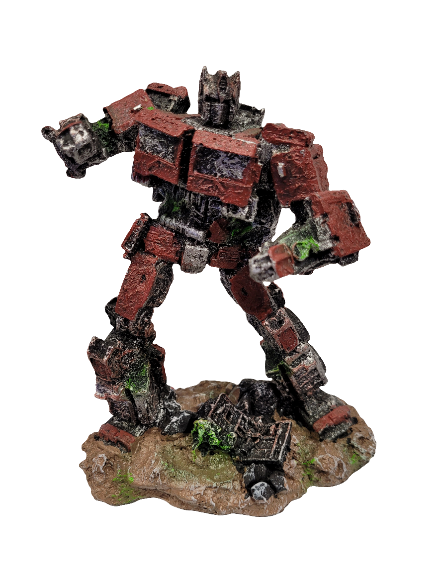 Standing on a rocky base, the Transformers Optimus Prime 7in. model features a rugged red and black design with weathered details. Its arms are positioned as if in motion, while green moss-like accents can be seen on both the ground and parts of the robot, enhancing its detailed appearance.