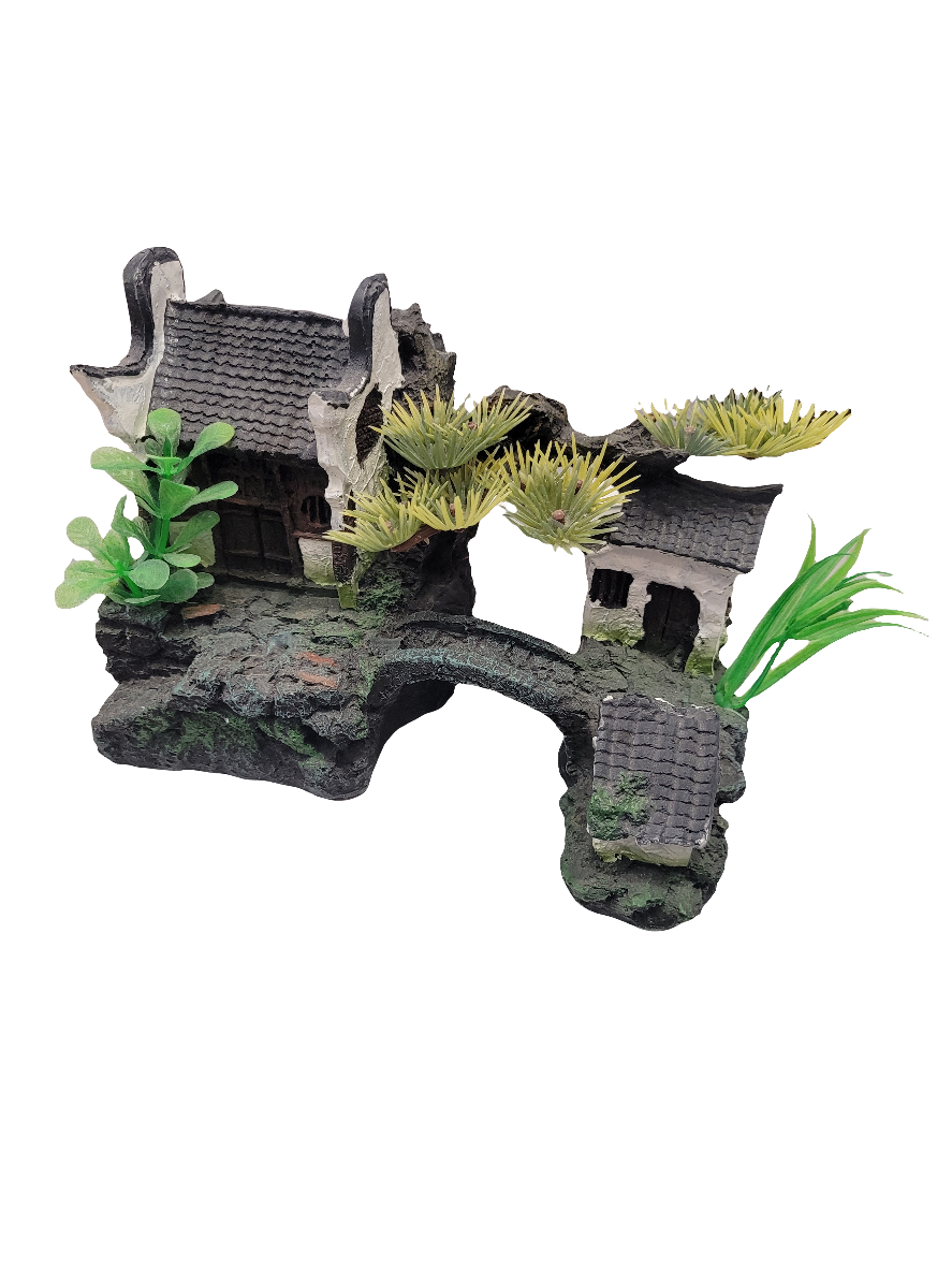 The White Casita with Bridge Decor - 7in wide is a rustic Asian-style miniature model featuring a stone bridge, artificial plants with green leaves and yellow spiky flowers, all set on a textured base resembling rock.